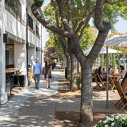 A man and woman walking down a street with tables and chairs.